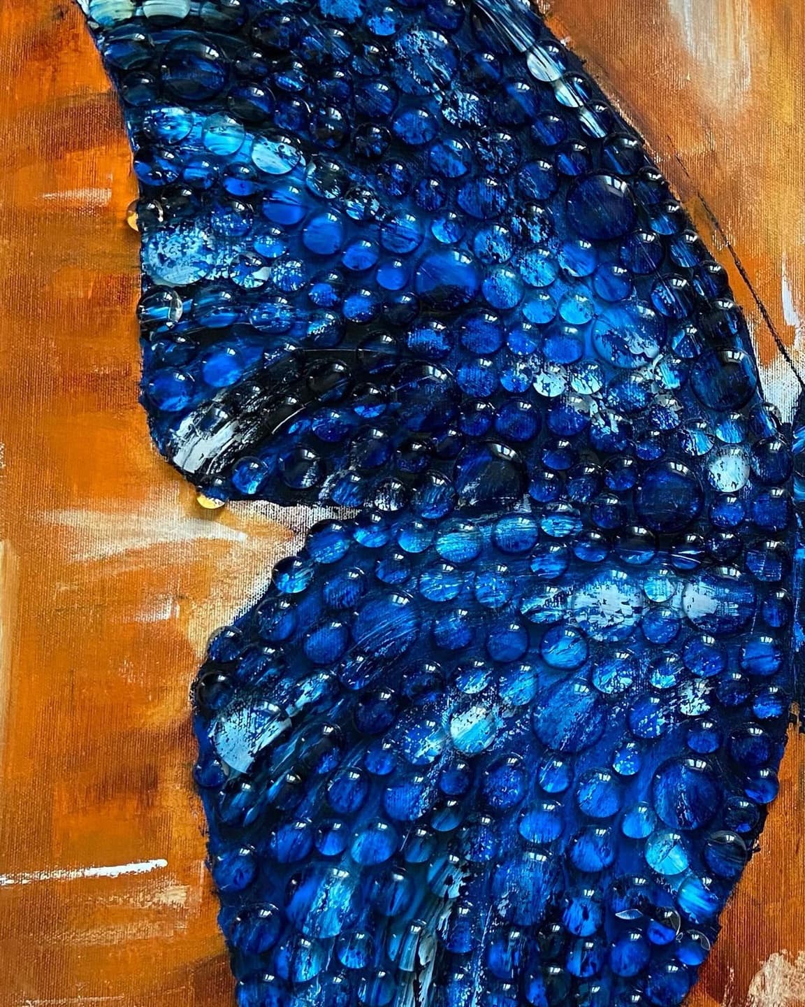 Close-up of the left wing covered in clear cast resin drops over blue paint.