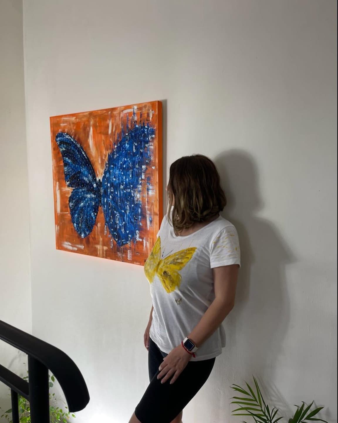 Helen She standing beside Butterfly Matrix Cristal hanging on a white wall.