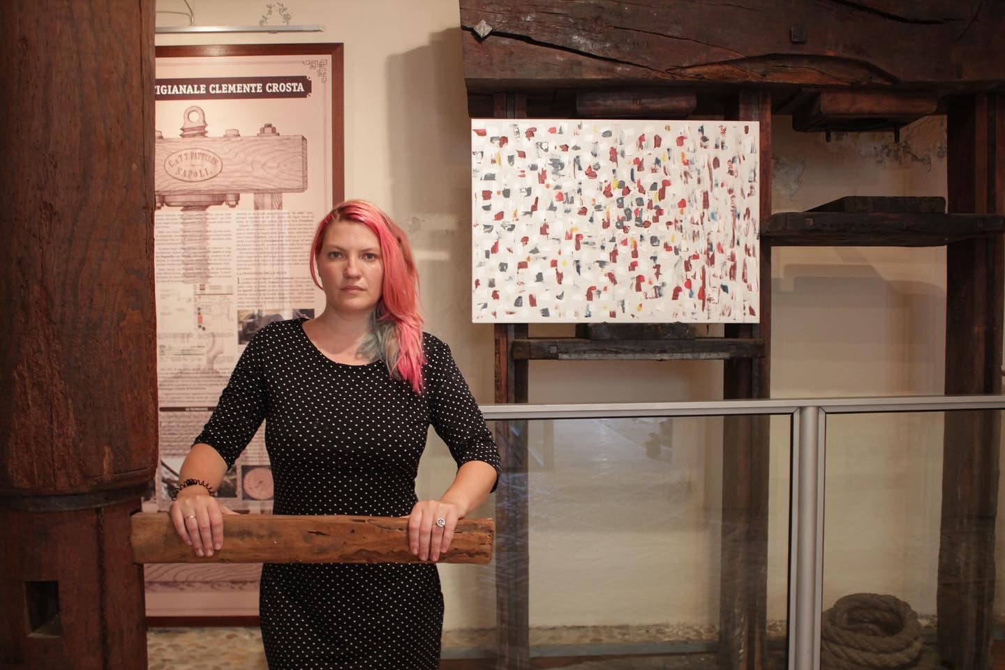 Helen She standing in front of one of her paintings under old wooden beams.