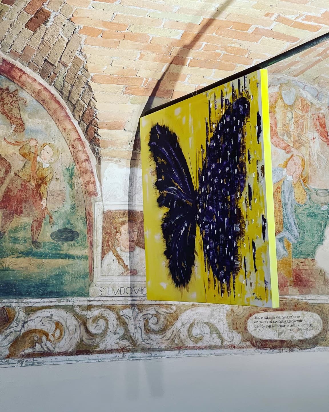 A purple butterfly on a yellow ground hung in front of old frescoes.