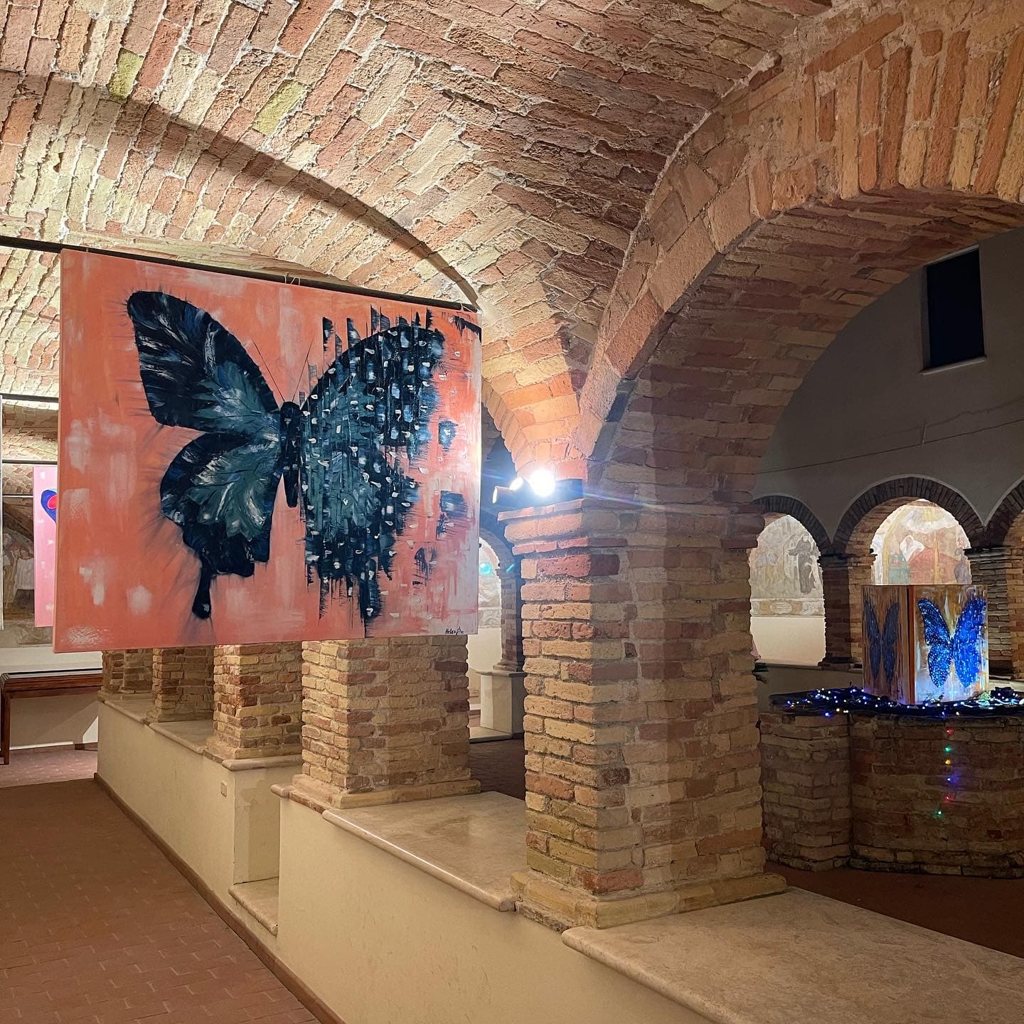 A butterfly painting on a coral ground hanging beneath brick vaults and columns.