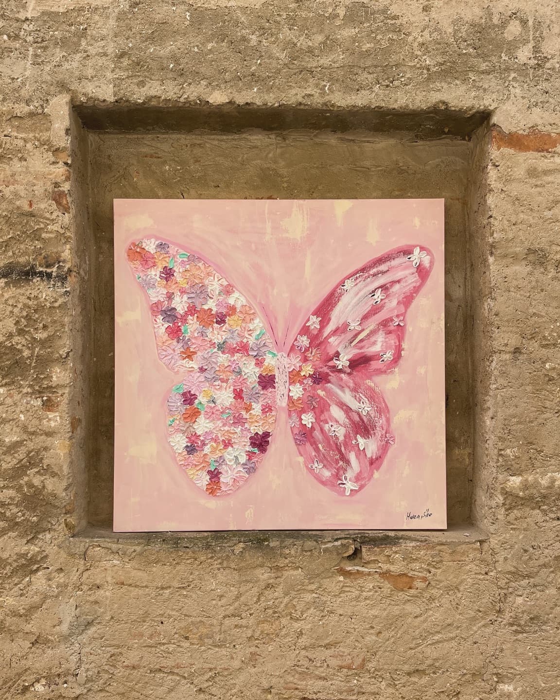 A pink butterfly painting set into a niche in an old brick wall.