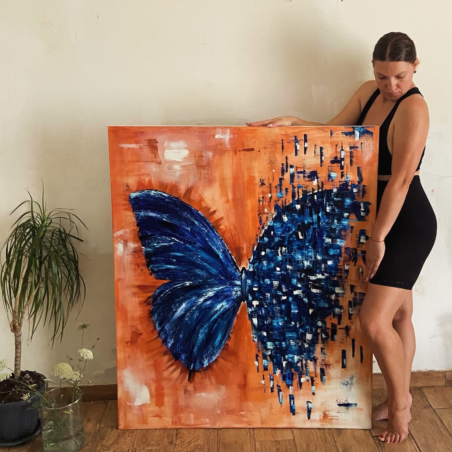Helen She holding a large canvas with a blue butterfly on an orange ground.