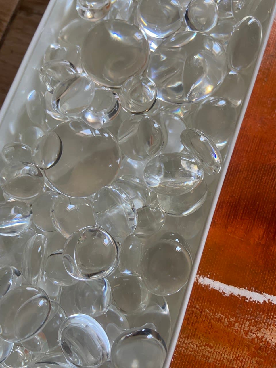 A white tray full of clear cast resin drops beside the orange-painted canvas.