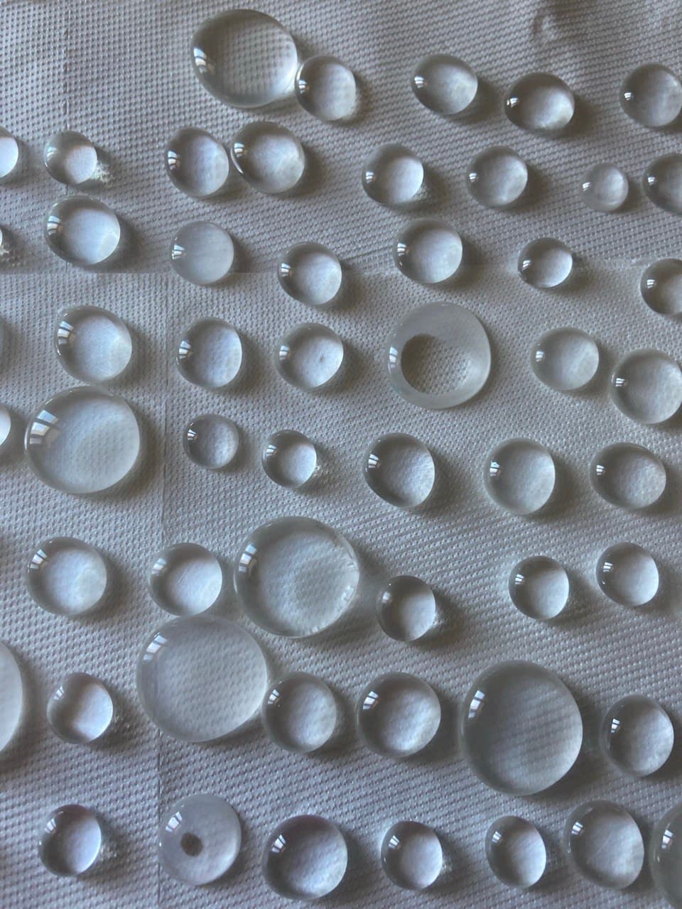 Clear cast drops of many different sizes laid out in rows on white paper.