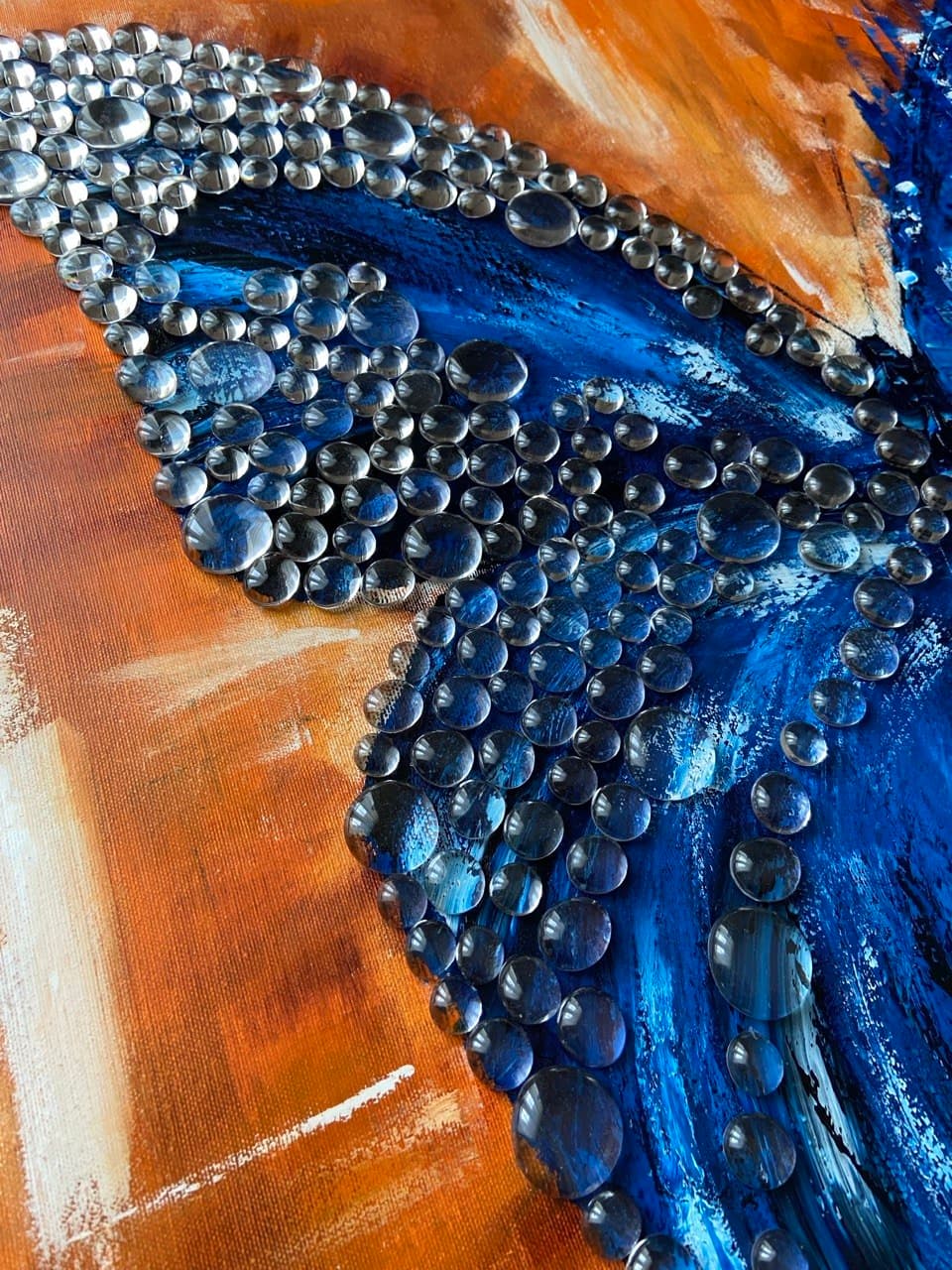 Clear drops arranged over the painted blue wing on the orange canvas.