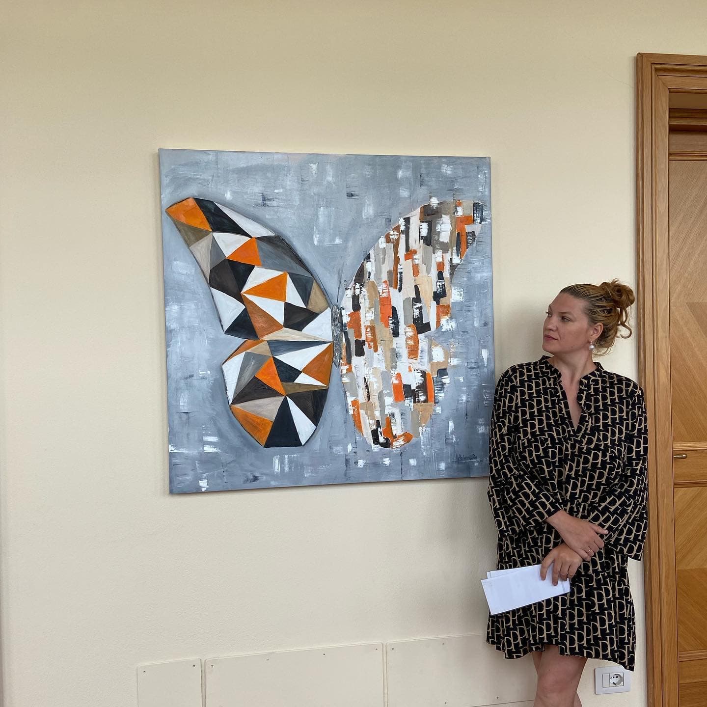 Helen She standing beside a large butterfly painting with a geometric wing.
